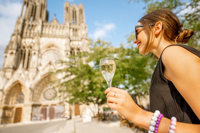 Young woman enjoying champagne standing in front of the cathedral in Reims city, capital of Champagne wine region, France